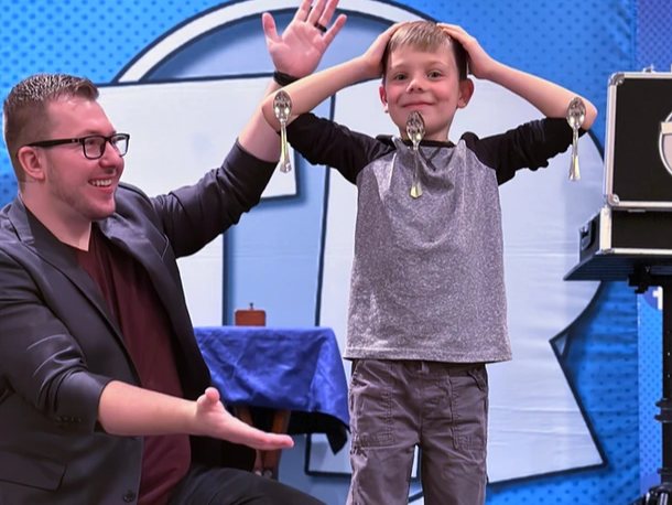A grinning kid stands with spoons hanging off him as Tyler presents him to the crowd