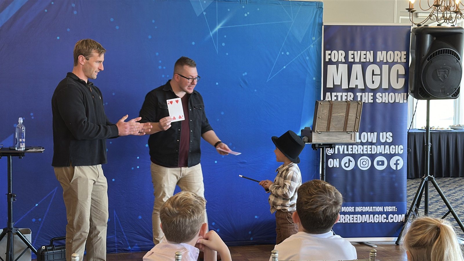 A young volunteer in a top hat waves the wand on stage while Tyler reveals the chosen card