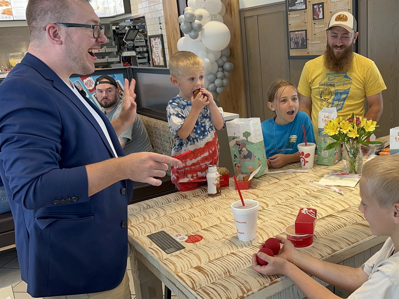 Kids and parents around a restaurant table react as the sponge balls appear in a boy's hands