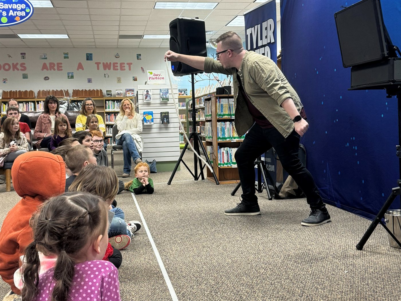 Kids sit on the floor between the shelves as Tyler works the rope routine