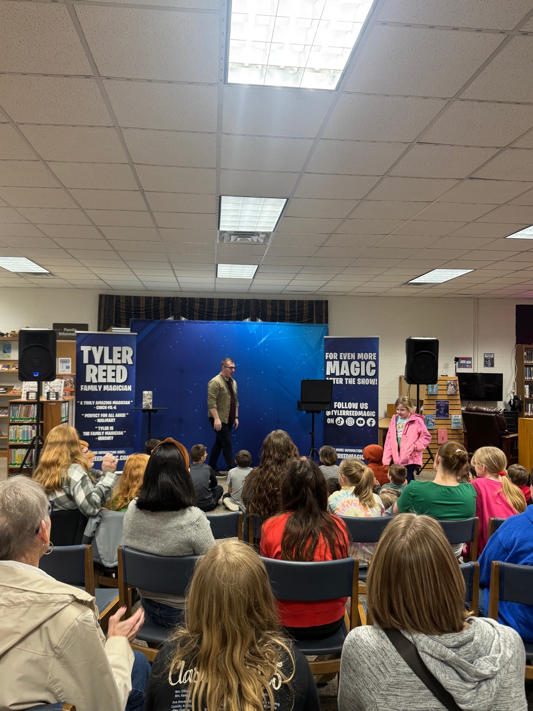 Families fill the library as Tyler performs in front of his blue stage backdrop