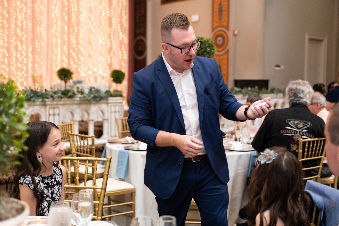 Tyler performs close-up magic for guests seated at a reception table